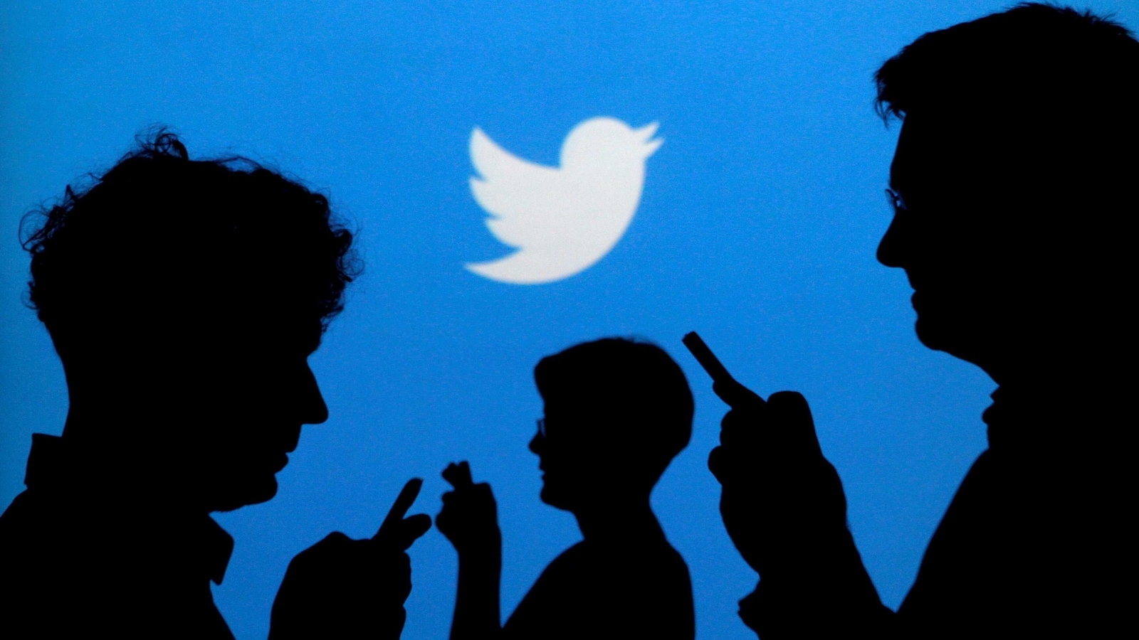 FILE PHOTO: People holding mobile phones are silhouetted against a backdrop projected with the Twitter logo in this illustration picture taken September 27, 2013. REUTERS/Kacper Pempel/Illustration/File Photo