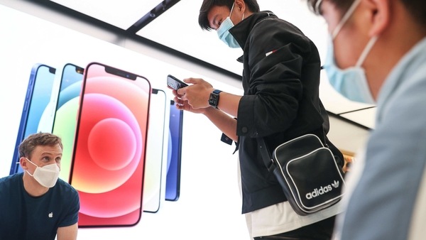 A customer wearing a protective mask tries out an Apple Inc. iPhone 12 Pro Max at the Apple flagship store during a product launch event in Sydney, Australia, on Friday, Nov. 13, 2020. Sales of the iPhone fell 21% on anticipation of the new models, which arrived later than usual this year. Cook said the response to the 5G iPhone lineup and other new devices has been 