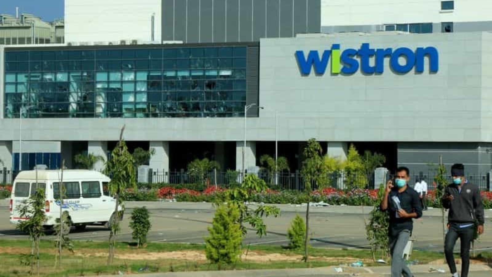 Men wearing protective face masks walk past broken windows of a facility run by Wistron Corp, a Taiwanese contract manufacturer for Apple, in Narsapura near the southern city of Bengaluru, India, December 14, 2020. REUTERS/Stringer