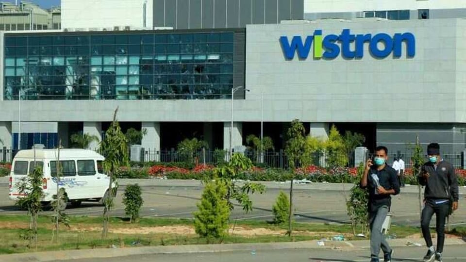 FILE PHOTO: Men wearing protective face masks walk past broken windows of a facility run by Wistron Corp, a Taiwanese contract manufacturer for Apple, in Narsapura near the southern city of Bengaluru, India, December 14, 2020. REUTERS/Stringer/File Photo