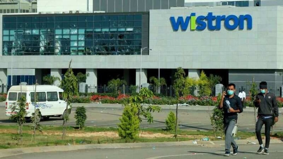 Men wearing protective face masks walk past broken windows of a facility run by the Wistron factory. Factory workers trashed the facilities over the weekend demanding unpaid wages and better working hours. 