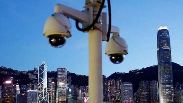A pair of surveillance cameras are seen along the Tsim Sha Tsui waterfront as skyline buildings stand across Victoria Harbor in Hong Kong, China.