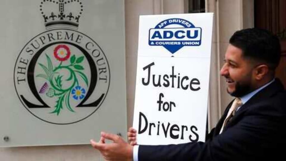 Uber driver and president of the (ADCU), App Drivers & Couriers Union, Yaseen Islam poses with a poster outside the Supreme Court in London, Friday, Feb. 19, 2021. The UK. Supreme Court ruled Friday that Uber drivers should be classed as “workers” and not self-employed.