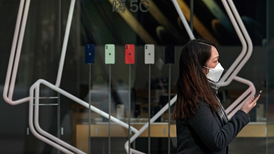 A woman wearing a face mask to help curb the spread of the coronavirus holds her smartphone as she passes an Apple store promoting its iPhone 12 devices powered with 5G at the capital city's popular shopping mall in Beijing on Wednesday, Feb. 24, 2021. (AP Photo/Andy Wong)