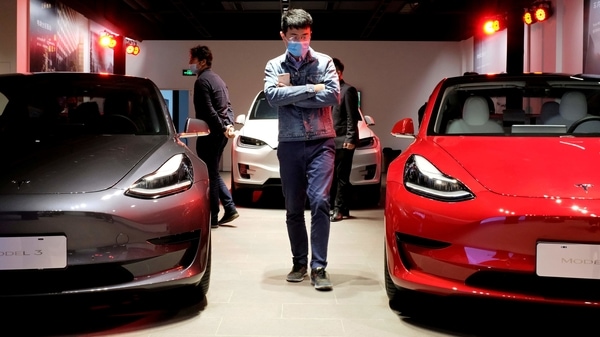 FILE PHOTO: A man wearing a face mask following the coronavirus disease (COVID-19) outbreak walks by Tesla Model 3 sedans and Tesla Model X sport utility vehicle at a new Tesla showroom in Shanghai, China May 8, 2020. REUTERS/Yilei Sun/File Photo