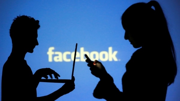 FILE PHOTO: People are silhouetted as they pose with laptops in front of a screen projected with a Facebook logo.