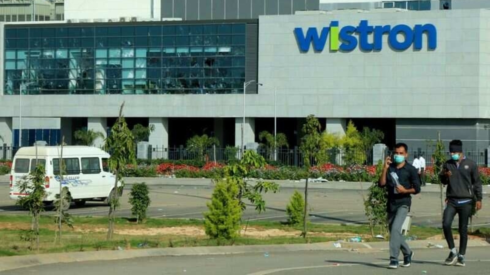 FILE PHOTO: Men wearing protective face masks walk past broken windows of a facility run by Wistron Corp, a Taiwanese contract manufacturer for Apple, in Narsapura near the southern city of Bengaluru, India, December 14, 2020. REUTERS/Stringer/File Photo