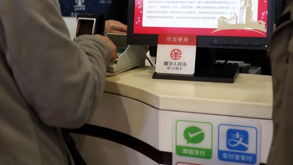 FILE PHOTO - A sign of China's digital yuan, or e-CNY, is seen above Wechat Pay and Alipay signs at a counter during a trial of the Digital Currency Electronic Payment (DCEP) at a shopping mall in Beijing, China February 10, 2021.