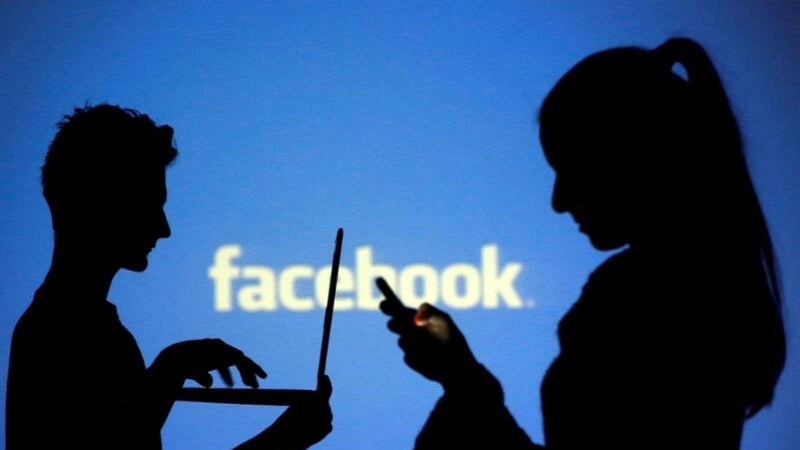 FILE PHOTO: People are silhouetted as they pose with laptops in front of a screen projected with a Facebook logo.