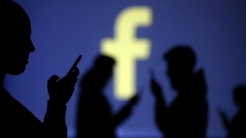 Silhouettes of mobile users are seen next to a screen projection of Facebook logo in this picture illustration taken March 28, 2018.  REUTERS/Dado Ruvic/Illustration