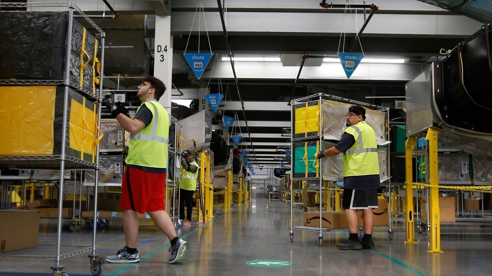 FILE - In this Dec. 17, 2019, file photo, Amazon workers move containers to delivery trucks at an Amazon warehouse facility in Goodyear, Ariz. Starting Monday, Aug. 9, 2021, Amazon will be requiring all of its 900,000 U.S. warehouse workers to wear masks indoors, regardless of their vaccination status.  The move follows steps by a slew of other retailers, including Walmart and Target, to mandate masks for their workers. In many of those cases the mandates apply to workers in locations of substantial COVID-19 transmission (AP Photo/Ross D. Franklin, File)