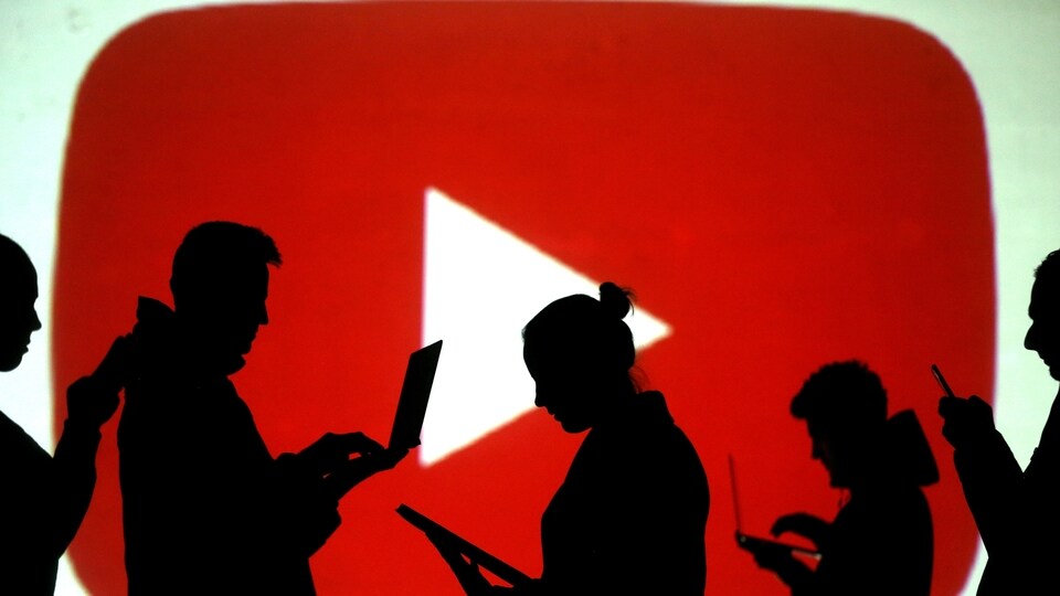 FILE PHOTO: Silhouettes of laptop and mobile device users are seen next to a screen projection of the YouTube logo in this picture illustration taken March 28, 2018.  REUTERS/Dado Ruvic/Illustration/File Photo