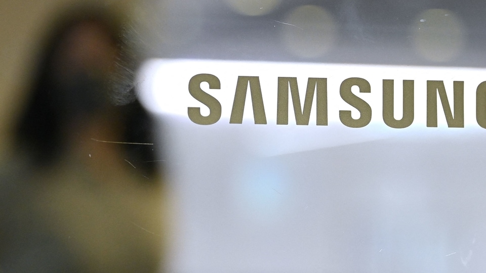 A woman walks past the Samsung logo displayed on a glass door at the company's Seocho building in Seoul on October 8, 2021 Samsung Galaxy S21 FE
