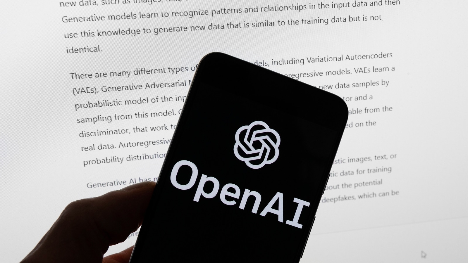 The OpenAI logo is seen on a mobile phone in front of a computer screen displaying output from ChatGPT, March 21, 2023, in Boston. OpenAI