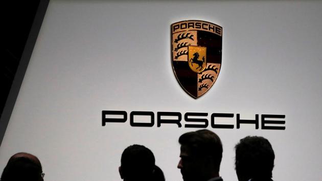 Visitors stand in front of a Porsche logo during the 88th Geneva International Motor Show in Geneva, Switzerland.