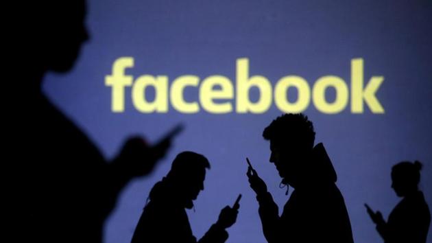 Silhouettes of mobile users are seen next to a screen projection of Facebook logo in this picture illustration taken March 28, 2018. REUTERS/Dado Ruvic/Illustration/File photo