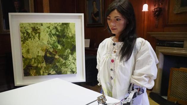 Robot artist 'Ai-Da' sketches using a pencil attached to her robotic arm, while standing next to a painting based on her computer vision data when run through algorithms developed by computer scientists in Oxford, Britain June 4, 2019.