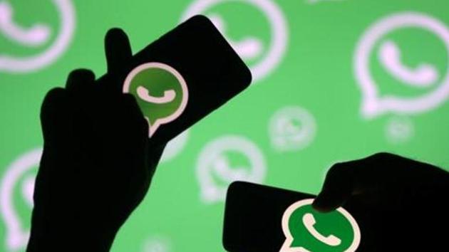 Men pose with smartphones in front of displayed Whatsapp logo.