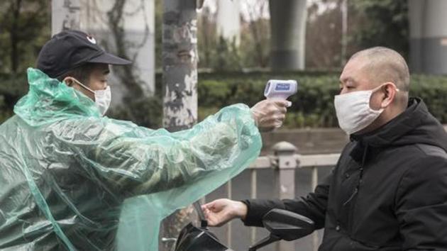 A security guard takes the temperature of a man wearing a protective mask at an entrance to a fresh produce market in Shanghai.