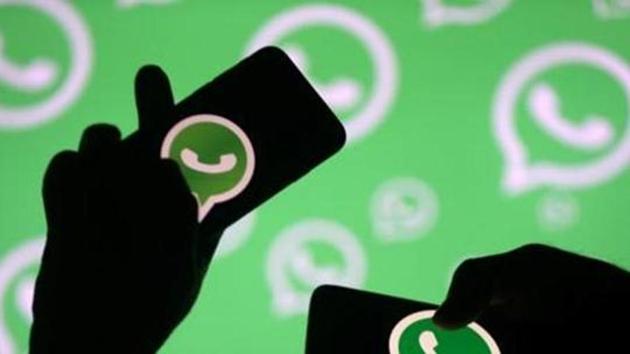 Men pose with smartphones in front of displayed Whatsapp logo in this illustration.