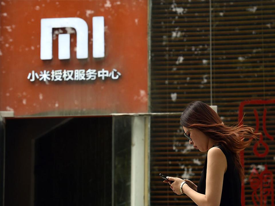 A woman walks past a Xiaomi logo outside a Xiaomi service center in Beijing