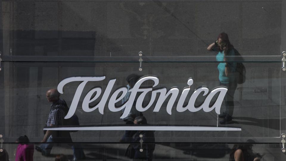 People are reflected in a glass sign of a Telefonica building in Madrid, Spain, Saturday, May 13, 2017. The Spanish government said several companies including Telefonica had been targeted in ransomware cyberattack that affected the Windows operating system of employees' computers.