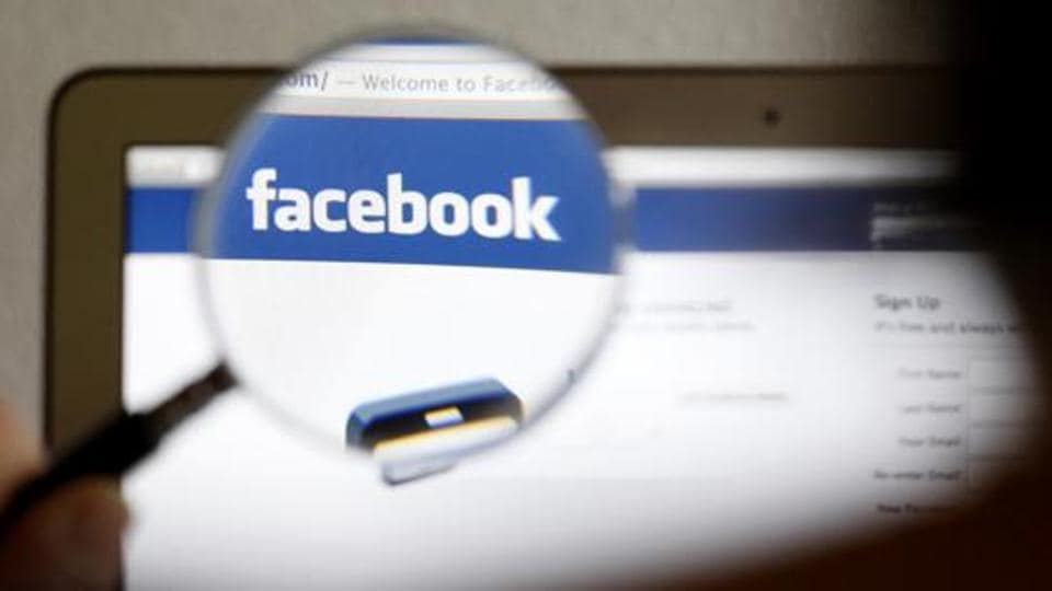 A Facebook logo on a computer screen is seen through a magnifying glass.