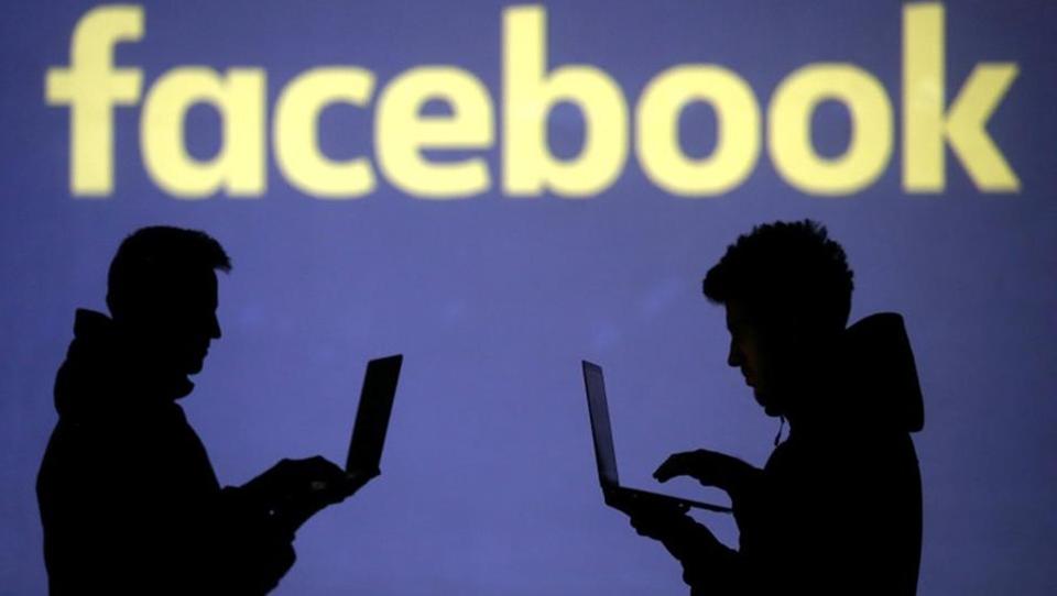 Silhouettes of laptop users are seen next to a screen projection of Facebook logo in this picture illustration taken on March 28.