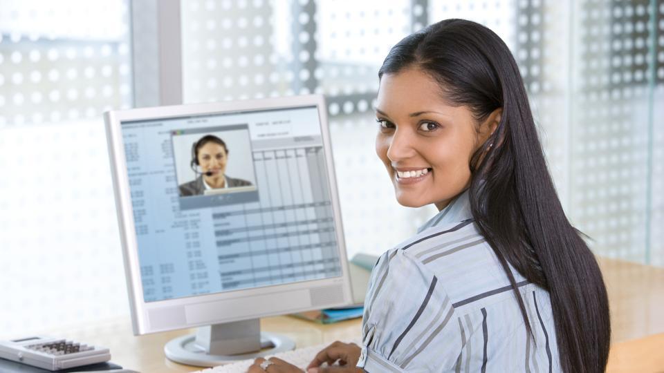 Young businesswoman, smiles back over her shoulder while on an internet video chat with a businessman. Horizontal shot.