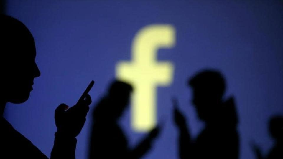 Silhouettes of mobile users are seen next to a screen projection of Facebook logo in this picture illustration taken March 28, 2018.