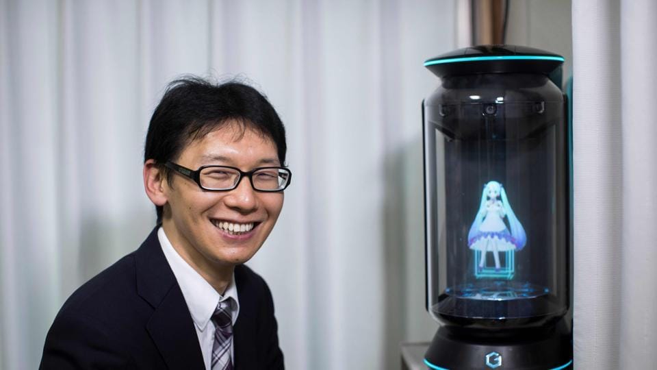 Akihiko Kondo poses next to a hologram of Japanese virtual reality singer Hatsune Miku at his apartment in Tokyo, a week after marrying her.
