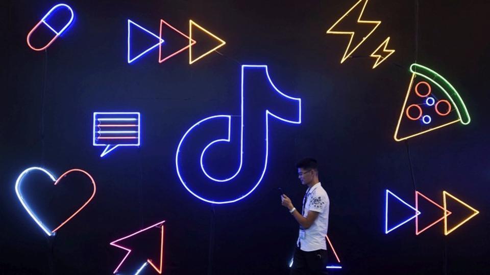 A man holding a phone walks past a sign of Chinese company ByteDance's app TikTok, known locally as Douyin, at the International Artificial Products Expo in Hangzhou, Zhejiang province, China October 18, 2019.