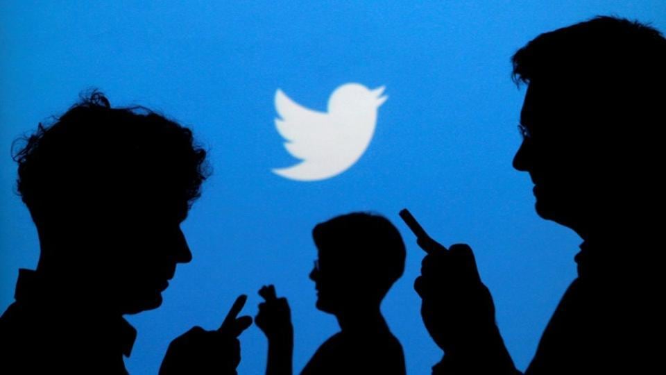 People holding mobile phones are silhouetted against a backdrop projected with the Twitter logo