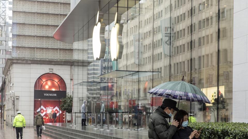 Pedestrians wearing protective masks use a smartphone under an umbrella in front of an Apple Inc. store in Shanghai, China, on Saturday, Feb. 15, 2020. China is entering the 