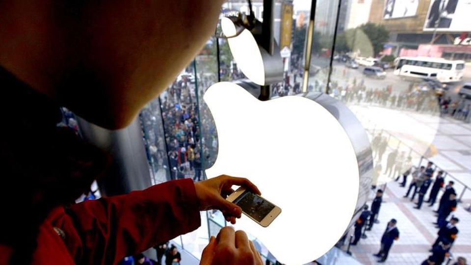 A man takes a photograph using his iPhone of members of the public entering an Apple store.