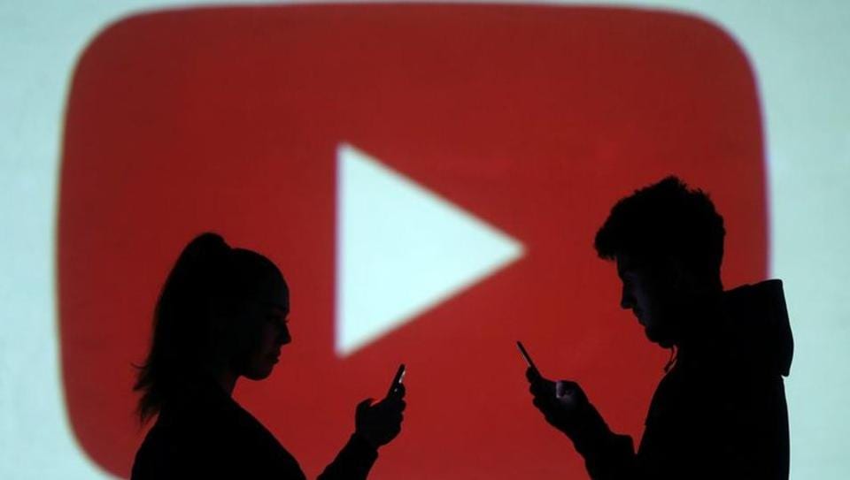 Silhouettes of mobile users are seen next to a screen projection of Youtube logo in this picture illustration taken March 28, 2018.