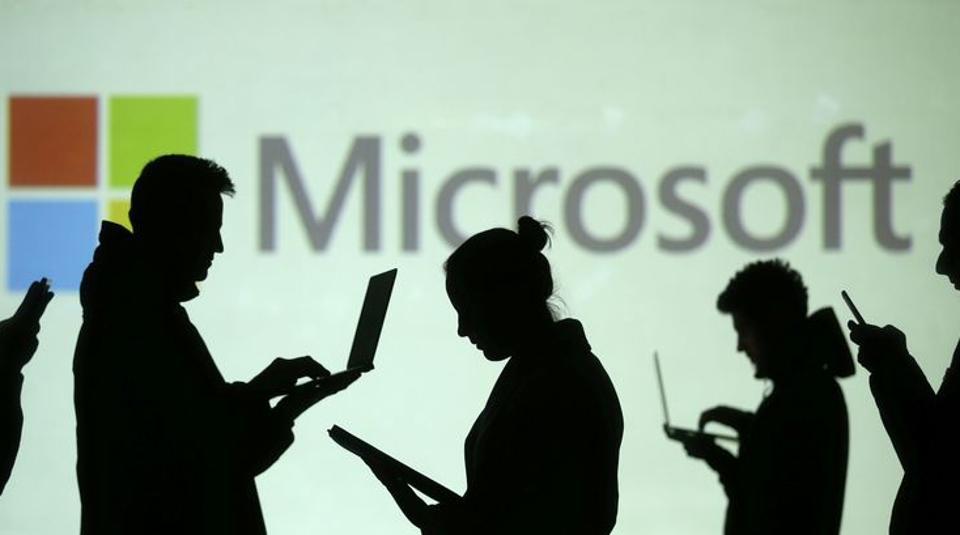 Silhouettes of laptop and mobile device users are seen next to a screen projection of Microsoft logo in this picture illustration taken March 28, 2018.