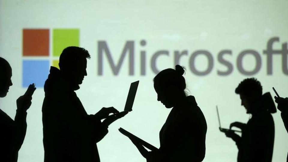 FILE PHOTO: Silhouettes of laptop and mobile device users are seen next to a screen projection of Microsoft logo in this picture illustration taken March 28, 2018.