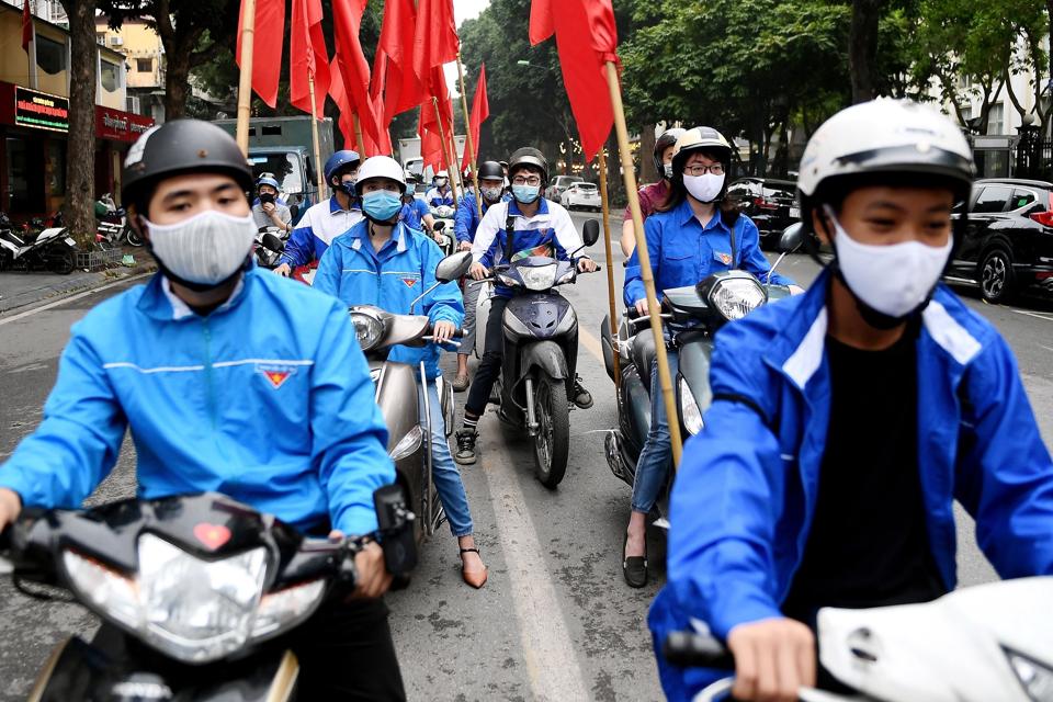People wearing face masks take part in a motorcade as a public awareness campaign for the prevention of the spread of COVID-19 novel coronavirus in Hanoi on March 23, 2020.