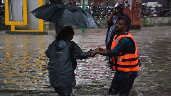 ముంబైలోని థానేలో నీట మునిగిన వీధుల గుండా ప్రయాణం చేస్తున్న వారికి సాయపడుతున్న సహాయక సిబ్బంది